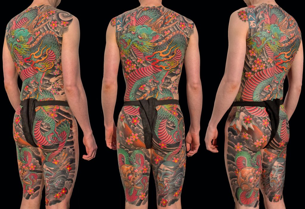 Three views of a person with extensive, colorful Japanese-style tattoos by Aaron Bell Tattoo Artist, covering their back, arms, and legs. The intricate designs depict dragons, flowers, and other elements. They are seen wearing a dark cloth around the waist.