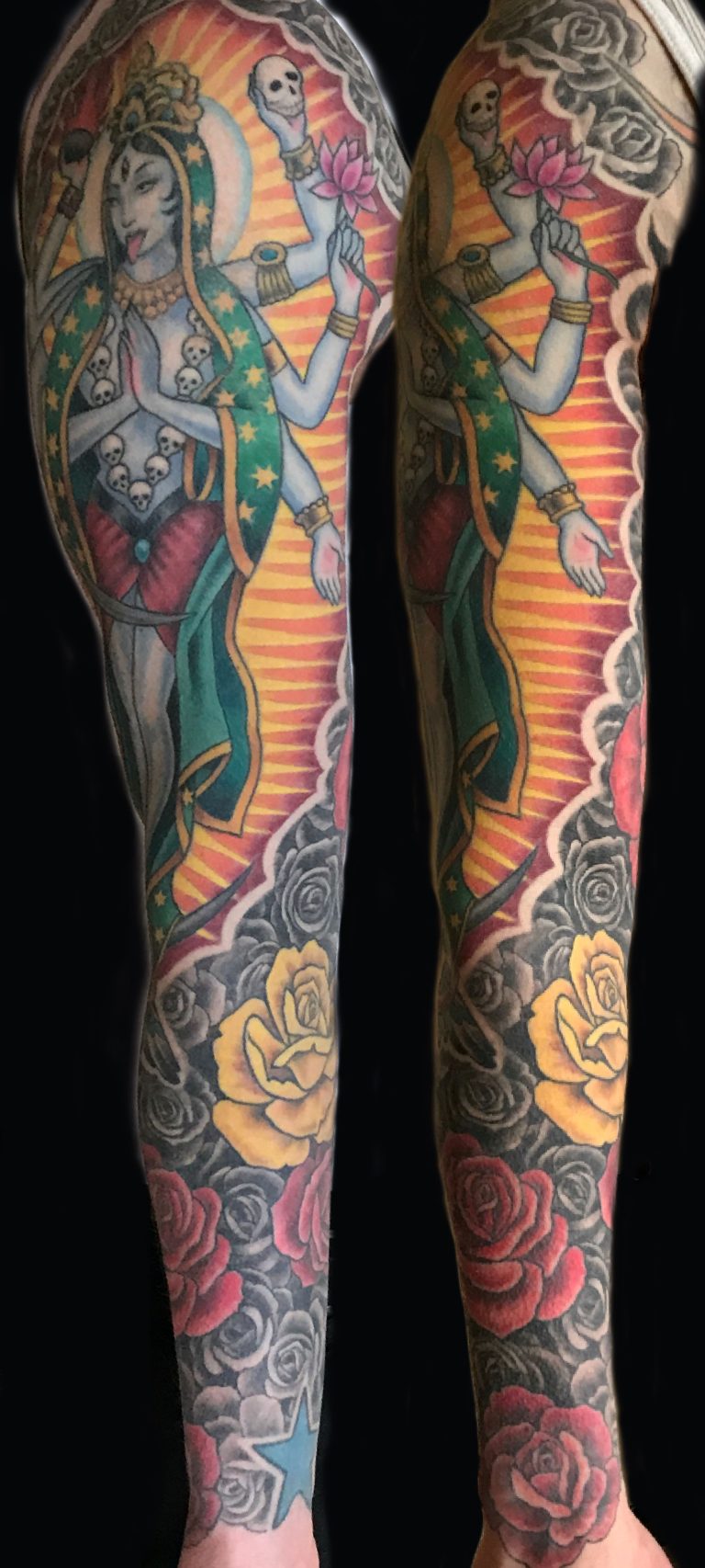 A colorful tattoo sleeve featuring a multi-armed deity holding a flower and a skull, surrounded by yellow and red roses with black and gray background shading.