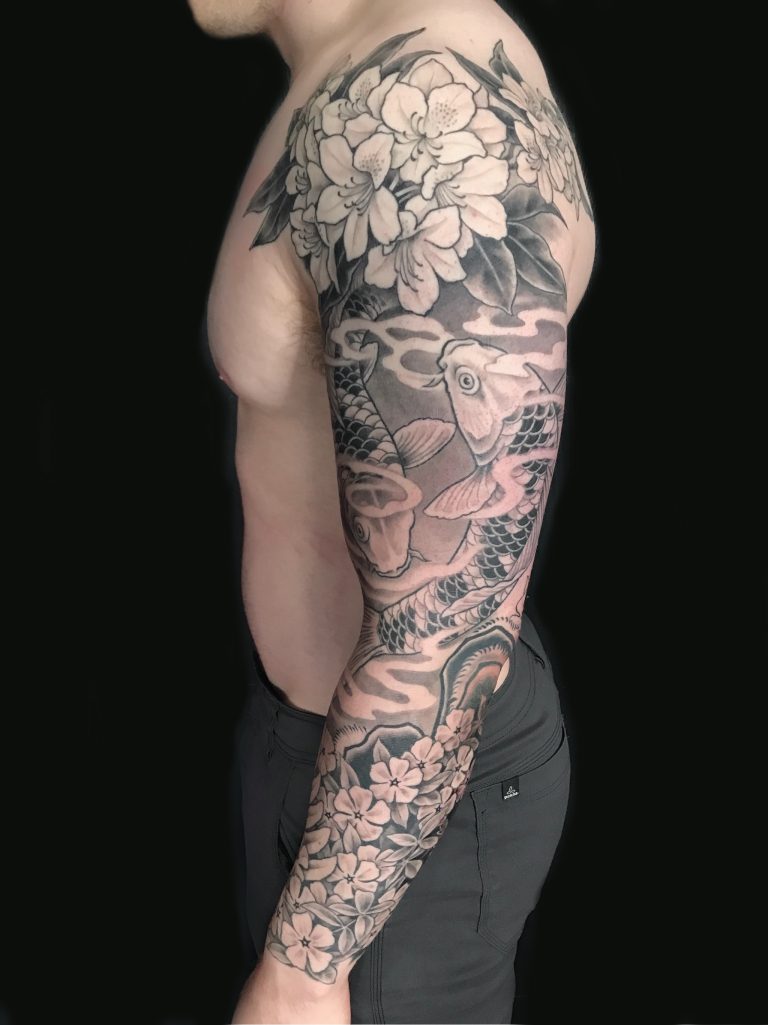 A person with a detailed black and gray sleeve tattoo featuring flowers and a koi fish.