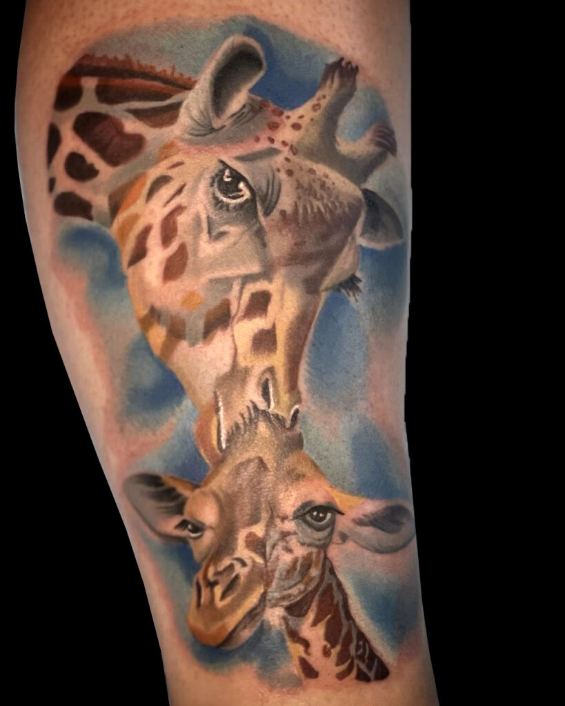 A realistic tattoo of two giraffes on a person's arm, with a colorful blue and brown background.