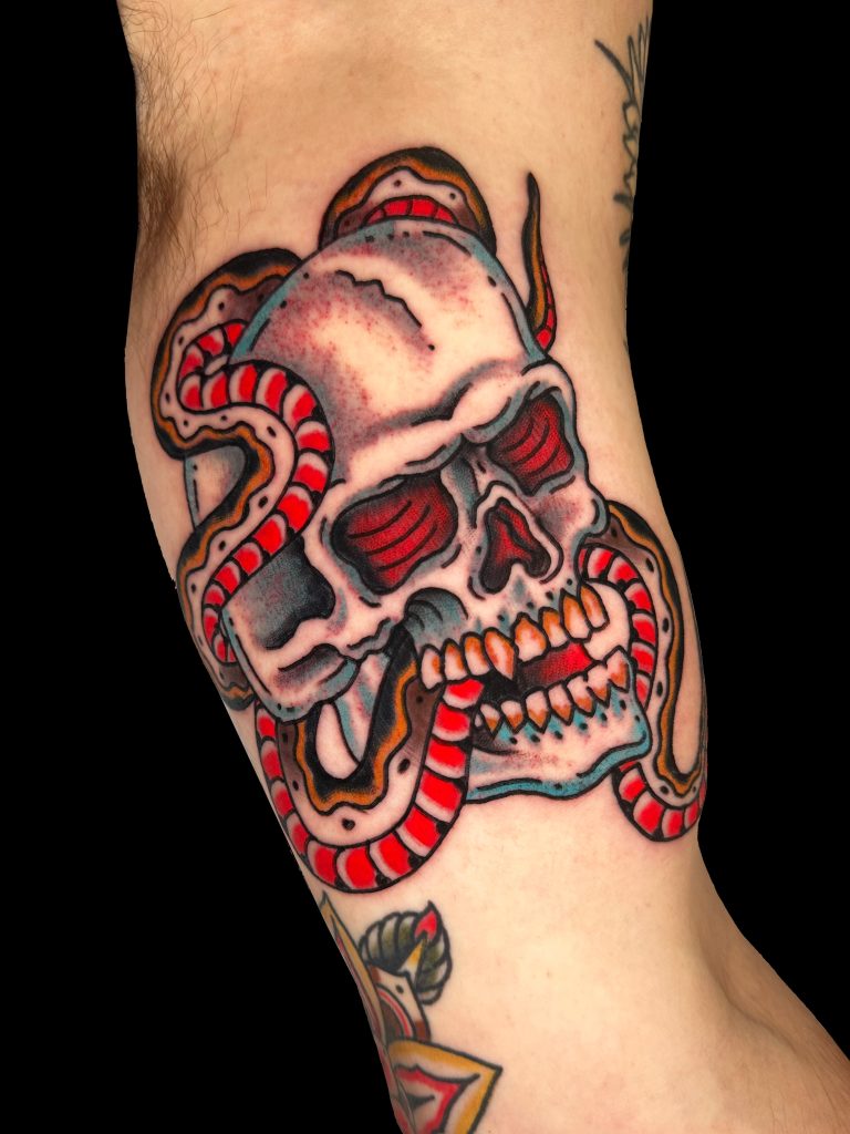 Tattoo of a skull with a snake wrapped around it, featuring red and white accents, on a person's arm.